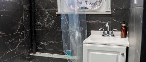 A bathroom with a bathtub, a sink, a mirror, and a fan.