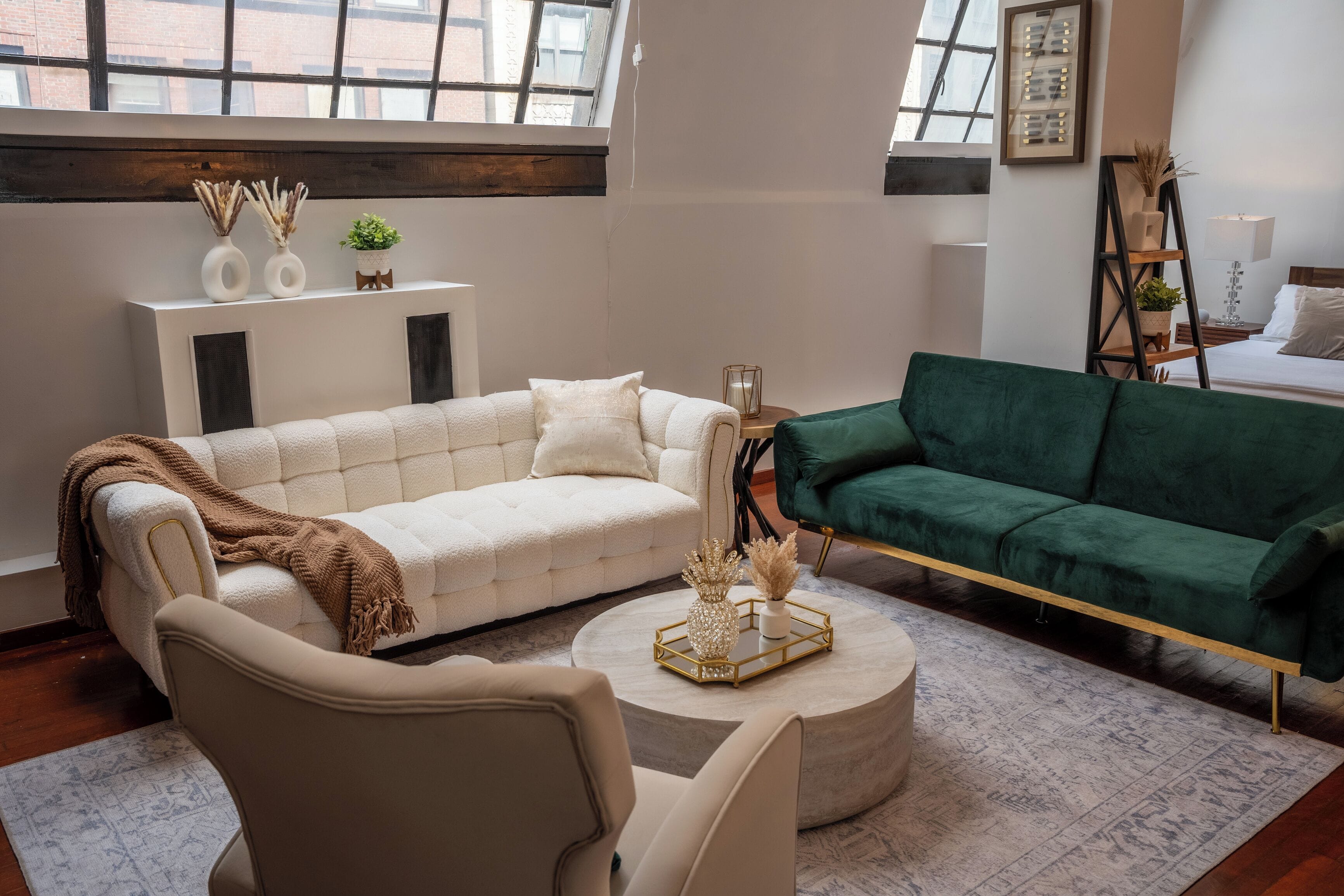 Una sala de estar con un sofá blanco, un sofá verde, una mesa redonda de centro con objetos decorativos y una chimenea con adornos en la pared.