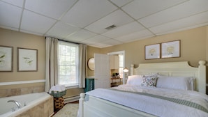 A bedroom with a large bed, a bathtub, and a window with curtains.