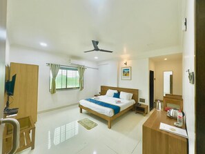 A hotel room with a bed, desk, chair, wardrobe, and a ceiling fan.