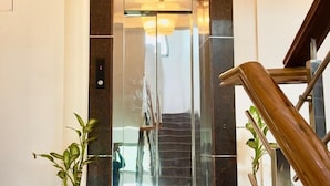 Un ascensore moderno con porta in vetro, una scala in legno e piante in vaso in un'accogliente hall luminosa.