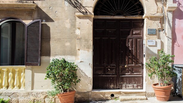 A building facade with a large wooden door, a window with shutters, and two potted plants. - Le dimore del mito - Atalanta (Syracuse)