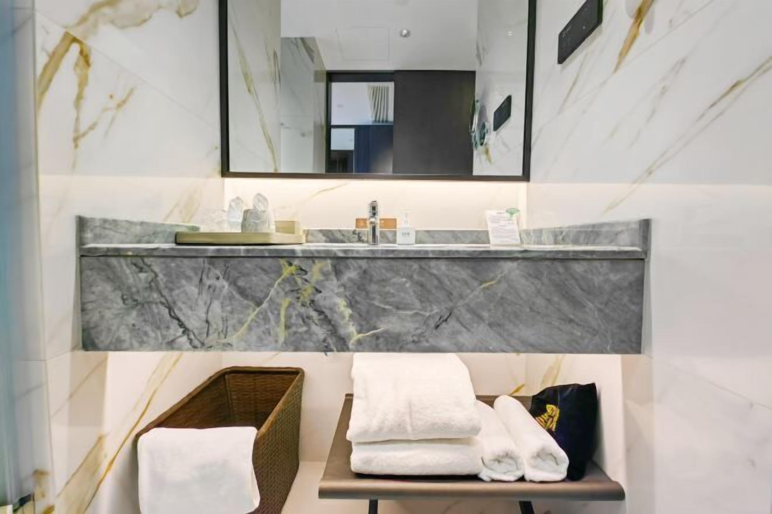A bathroom with a marble sink, a mirror, a towel rack, and a basket.