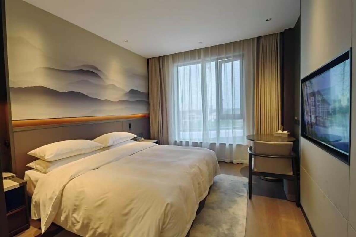 A hotel room with a large bed, a desk, a chair, and a TV.
