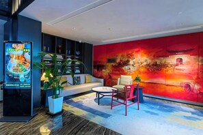 Een moderne hotel lobby met een groot digitaal menu bord, een bank, een bijzettafeltje en een levendige rode muur met abstracte kunst.