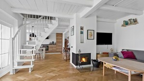 A spacious living area with a wooden herringbone floor, a fireplace, a television mounted on the wall, and a staircase leading to an upper level. - 3 bedroom beautiful home in Holbæk (Holbæk)
