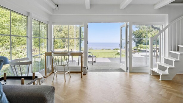 A spacious room with large windows, a wooden floor, and a view of the outdoors. - 3 bedroom beautiful home in Holbæk (Holbæk)