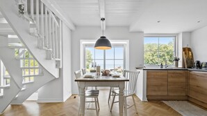 A spacious dining area with a wooden table and chairs, a large window with a view, and a staircase with white railings. - 3 bedroom beautiful home in Holbæk (Holbæk)