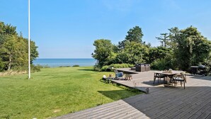 A wooden deck with outdoor furniture, a grassy lawn, and a view of the sea. - 3 bedroom beautiful home in Holbæk (Holbæk)