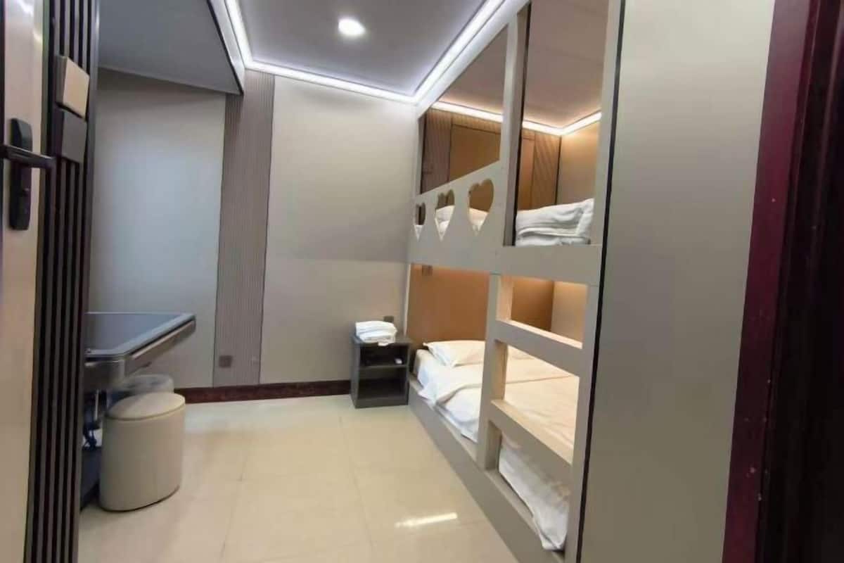 Una habitación con literas, un escritorio, una silla, una mesita y un cubo de basura.