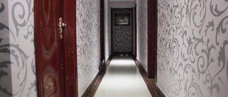 A corridor with patterned wallpaper, a wooden door, and a framed picture on the wall.