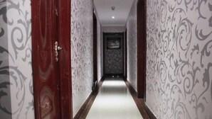 Un pasillo con papel tapiz estampado, una puerta de madera y suelo de baldosas.