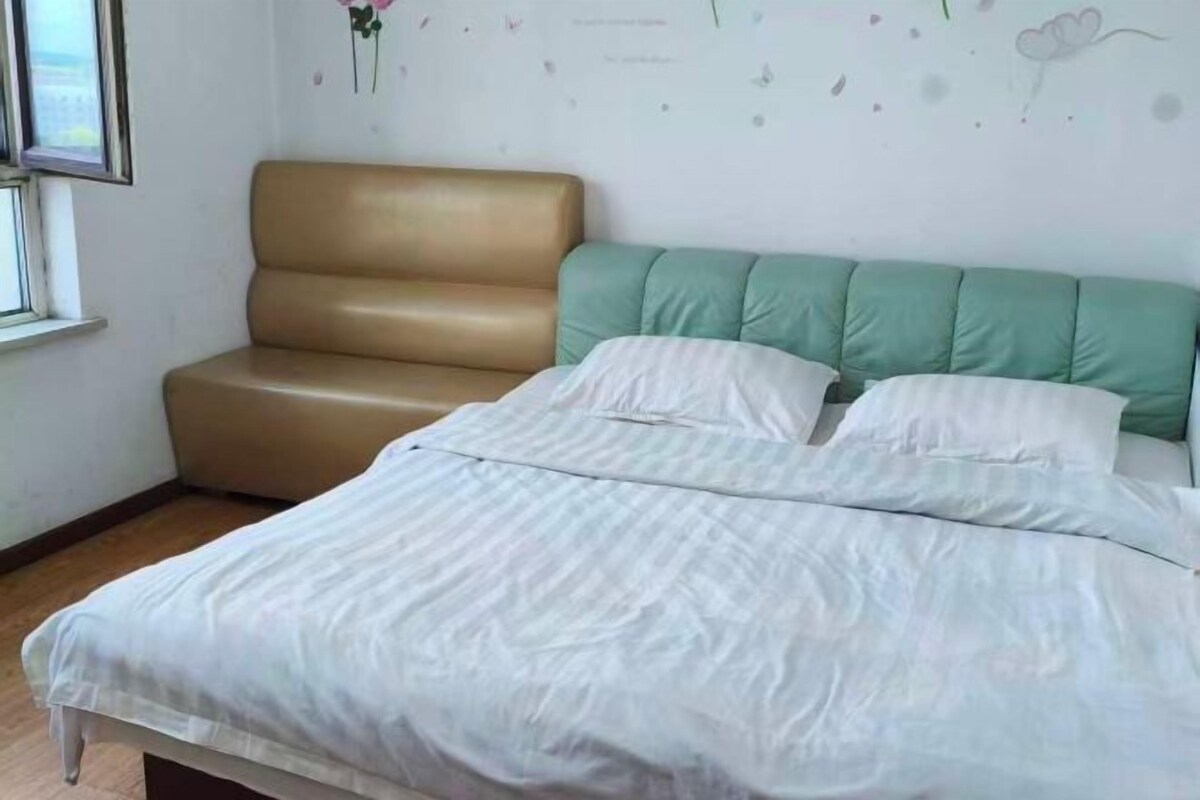 A bed with white bedding, a green headboard, and a brown chair.