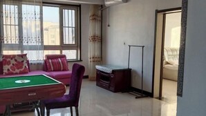 Una habitación con mesa de billar, un sofá morado, un aparador de madera y una cama al fondo.