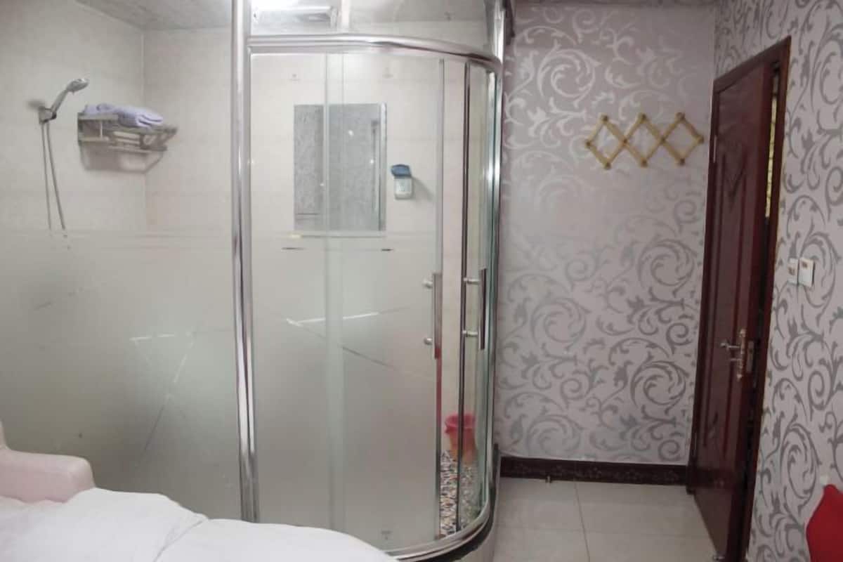 Habitación con cabina de ducha de vidrio, cama, puerta y papel tapiz estampado.