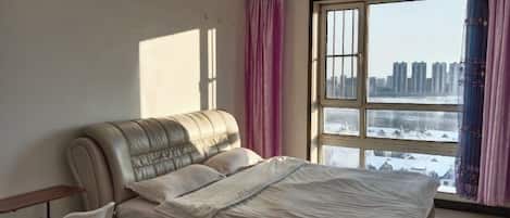 Un dormitorio con una cama, una silla y un gran ventanal con cortinas.