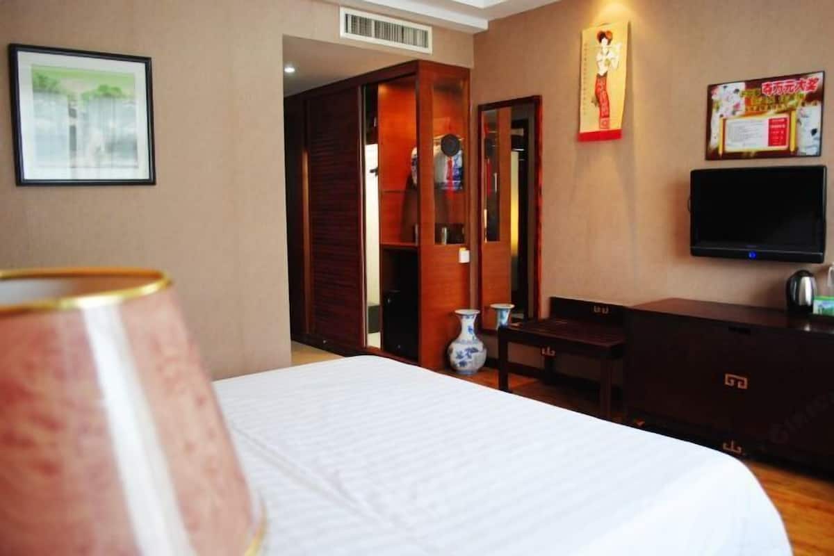 Une chambre d’hôtel avec un lit, une télévision, une armoire en bois et un vase.