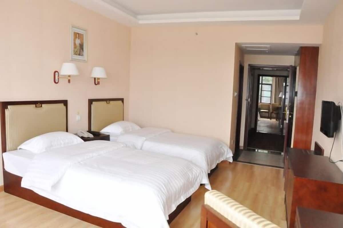Une chambre d’hôtel avec deux lits, un bureau, une chaise, une télévision et une porte donnant sur une autre pièce.