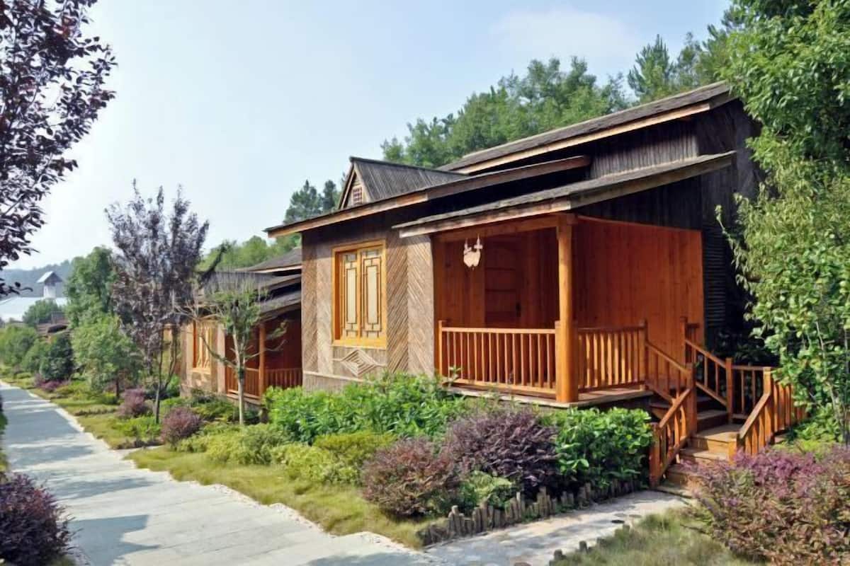 Une rangée de cabanes en bois dotées d’un porche, entourées de verdure et baignées par un ciel dégagé.