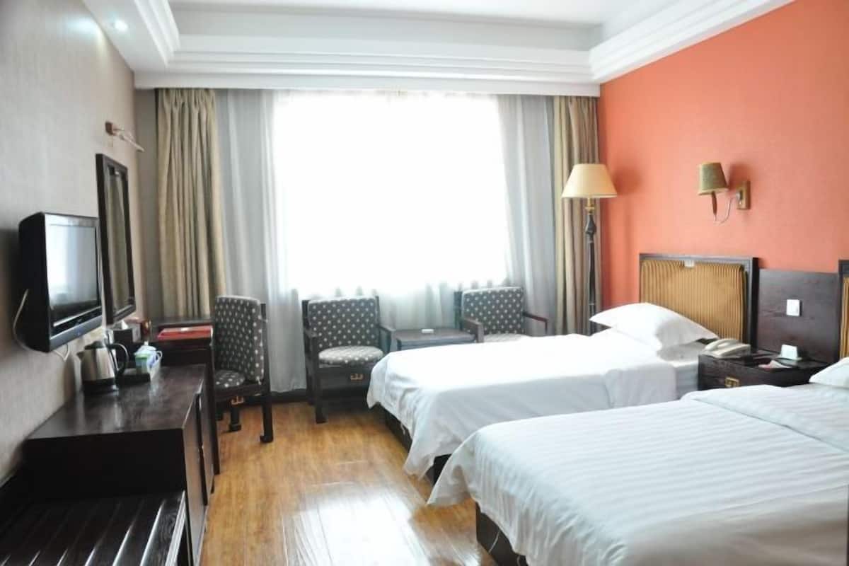 Une chambre d’hôtel avec deux lits, un bureau avec une télévision, une chaise, une lampe et une fenêtre avec des rideaux.