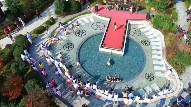 Une piscine circulaire dotée d’une terrasse rouge, entourée d’un sentier en pierre et de bancs.