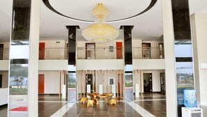Un hall d’entrée spacieux avec un plafond haut, un lustre central et un espace détente avec des bancs en bois.