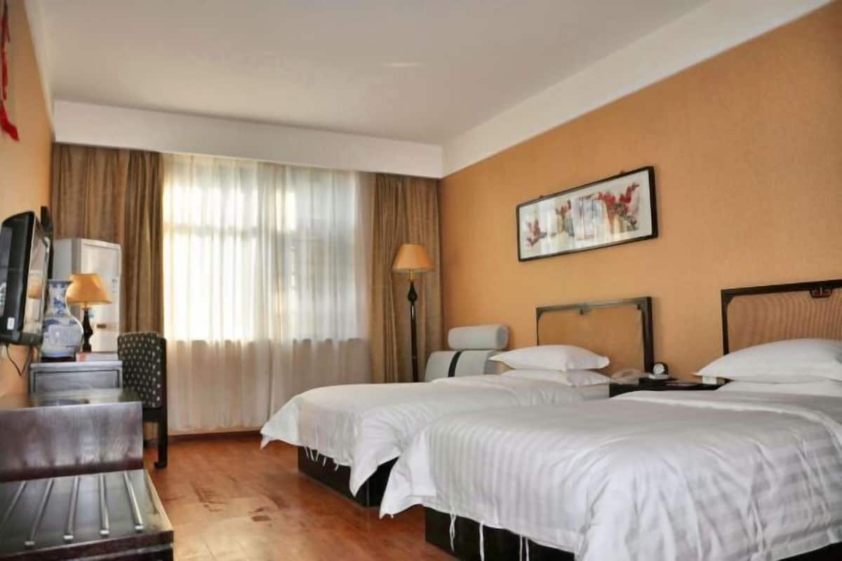 Une chambre d’hôtel avec deux lits, un bureau avec une chaise, une télévision et une lampe.