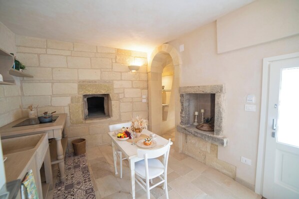 A kitchen with a stone wall, a fireplace, and a dining table set for two. - Trullo Meraviglia With Garden And Pool (Castrignano de' Greci)