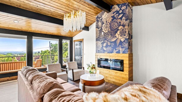 A modern living room with a large sofa, a fireplace, and a balcony with a view. - Premier Montana Retreat | River + Mountain Views | W & R (Great Falls)