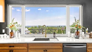 A kitchen with a large window, a sink, and wooden cabinets. - Premier Montana Retreat | River + Mountain Views | W & R (Great Falls)