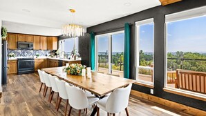 A modern kitchen with wooden cabinets, a large dining table, and a view of the outdoors. - Premier Montana Retreat | River + Mountain Views | W & R (Great Falls)