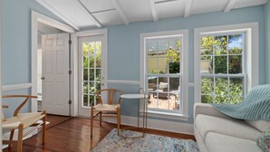 A room with a wooden floor, a white door, a window with a view of a garden, and a white sofa with a blue blanket. - Casa Amarillo l Steps to Historic District (St. Augustine)