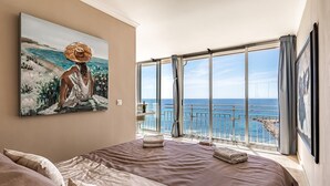 A bedroom with a large bed, a painting of a woman by the sea, and a balcony with a view of the ocean and a bridge. - Altea Bahia - Altea, Costa Blanca (Altea)