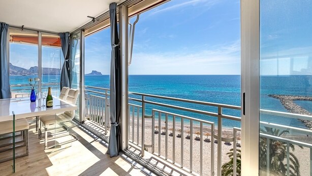 A balcony with a glass door, a table with a bottle and glasses, and a view of the sea and rocky coastline. - Altea Bahia - Altea, Costa Blanca (Altea)