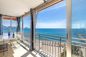 A balcony with a glass door, a table with a bottle and glasses, and a view of the sea and rocky coastline. - Altea Bahia - Altea, Costa Blanca (Altea)