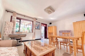 Ein Zimmer mit einem Bett, einem Holztisch, Stühlen, einem Schreibtisch und einem Fenster mit Vorhängen.