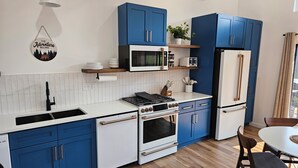 Uma cozinha moderna com armários azuis, bancada branca, fogão, micro-ondas e geladeira.