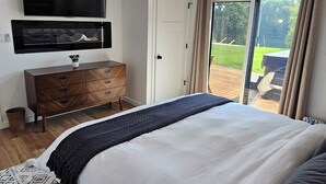Quarto com uma cama grande, ventilador de teto, TV fixada na parede e porta de vidro deslizante para área externa.