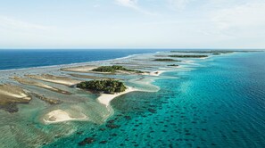 An aerial view of a coastal area with clear blue waters, sandy beaches, and small islands with vegetation. - Location Maison Entière a 5 Minutes à Pied D'une Plage (Rangiroa)