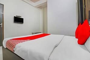 Ein Hotelzimmer mit Bett, Wandfernseher und rotem Kopfkissen.
