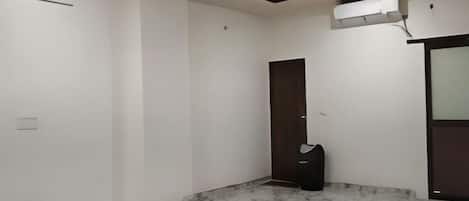 A room with a marble floor, a dark door, and a wall-mounted air conditioning unit.