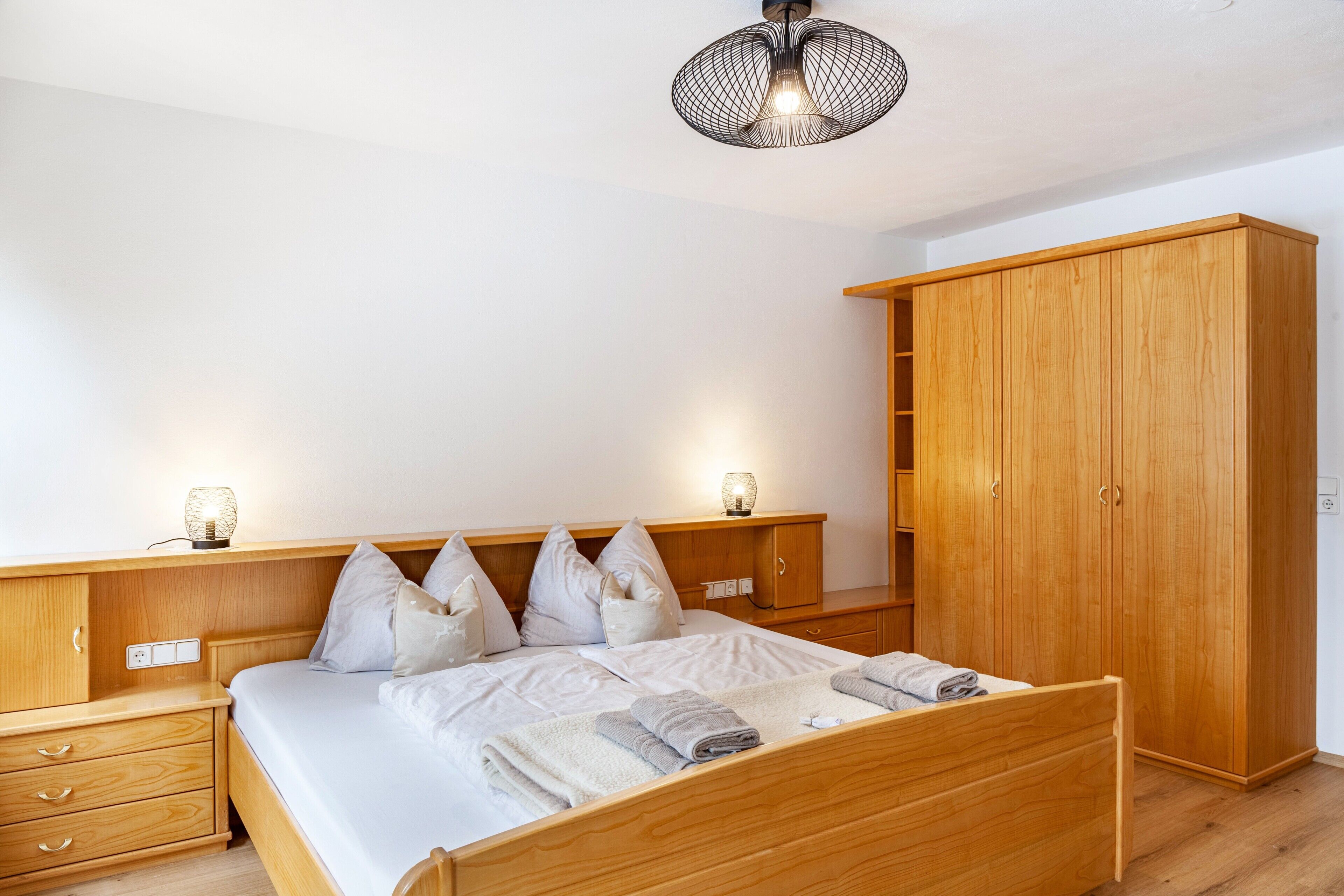A bedroom with a wooden bed, bedside tables, a wardrobe, and a hanging light fixture.