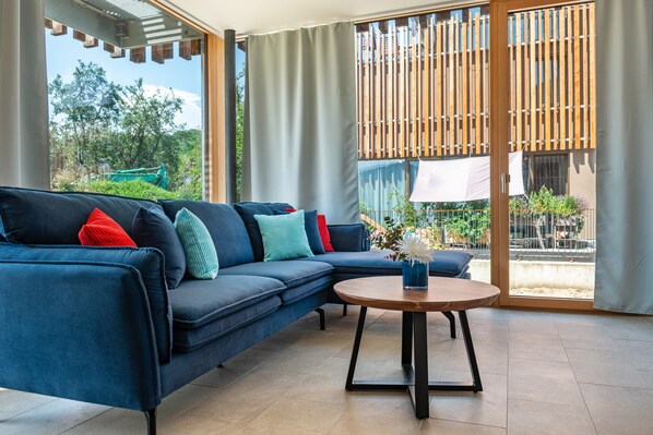 A modern living room with a blue sofa, a round coffee table, and a view of greenery outside.