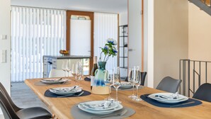A dining area with a wooden table set for six, a vase with flowers, and a kitchen in the background. - Holiday Home 'Architektenhaus C1 Mit Seesicht' with Lake View, Private Terrace and Wi-Fi (Öhningen)