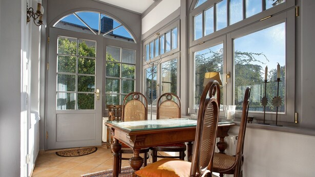 A dining area with a glass-top table, wooden chairs, and a view through large windows. - Villa 'Effi-Briest-' with Mountain View, Private Terrace and Wi-Fi (Ostseebad Heringsdorf)
