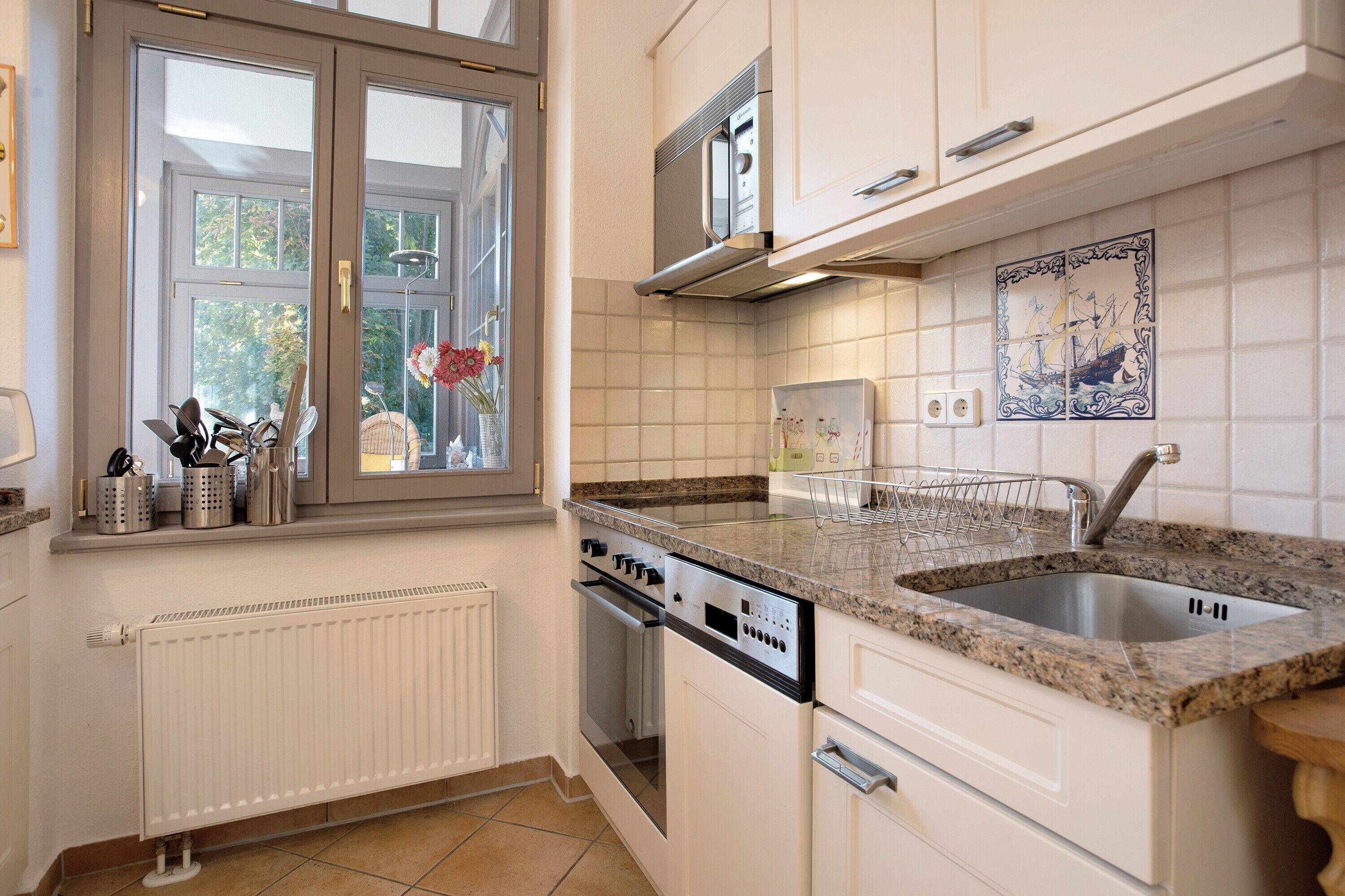 Eine Küche mit Fenster, weißen Schränken, einer Mikrowelle, einem Geschirrspüler und einer Spüle.