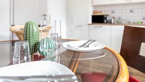 Un tavolo da pranzo con piano in vetro, circondato da sedie, in una cucina moderna con pensili bianchi e un forno a microonde.