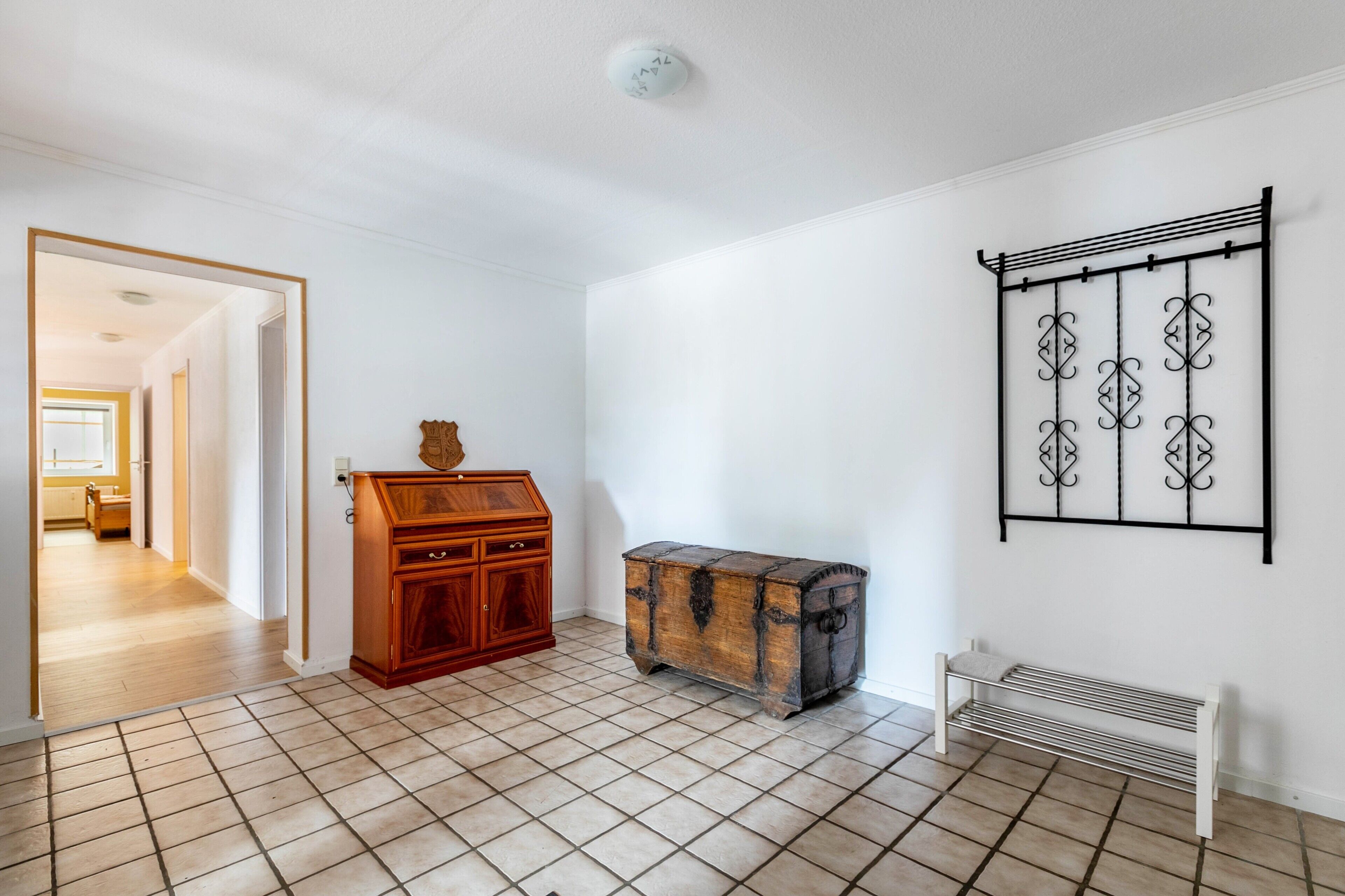 Una habitación con un armario de madera, un perchero metálico de pared y un banco.