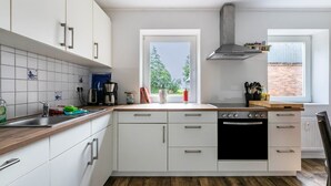 Cucina con mobili bianchi, un piano di lavoro in legno, un fornello e una finestra con vista sul verde.