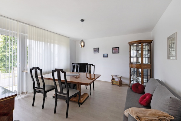 Un coin repas avec une table et des chaises en bois, un canapé avec des coussins rouges et un buffet en bois.